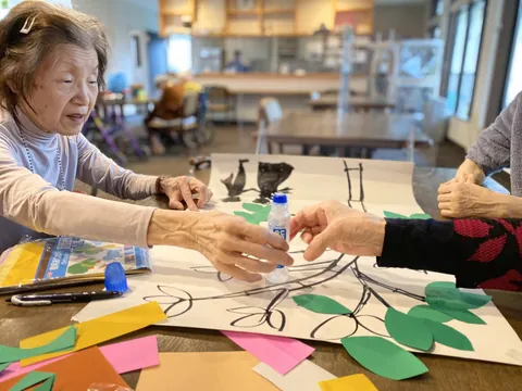 テーブルで色紙の制作を楽しみ、のりを手渡す人たち